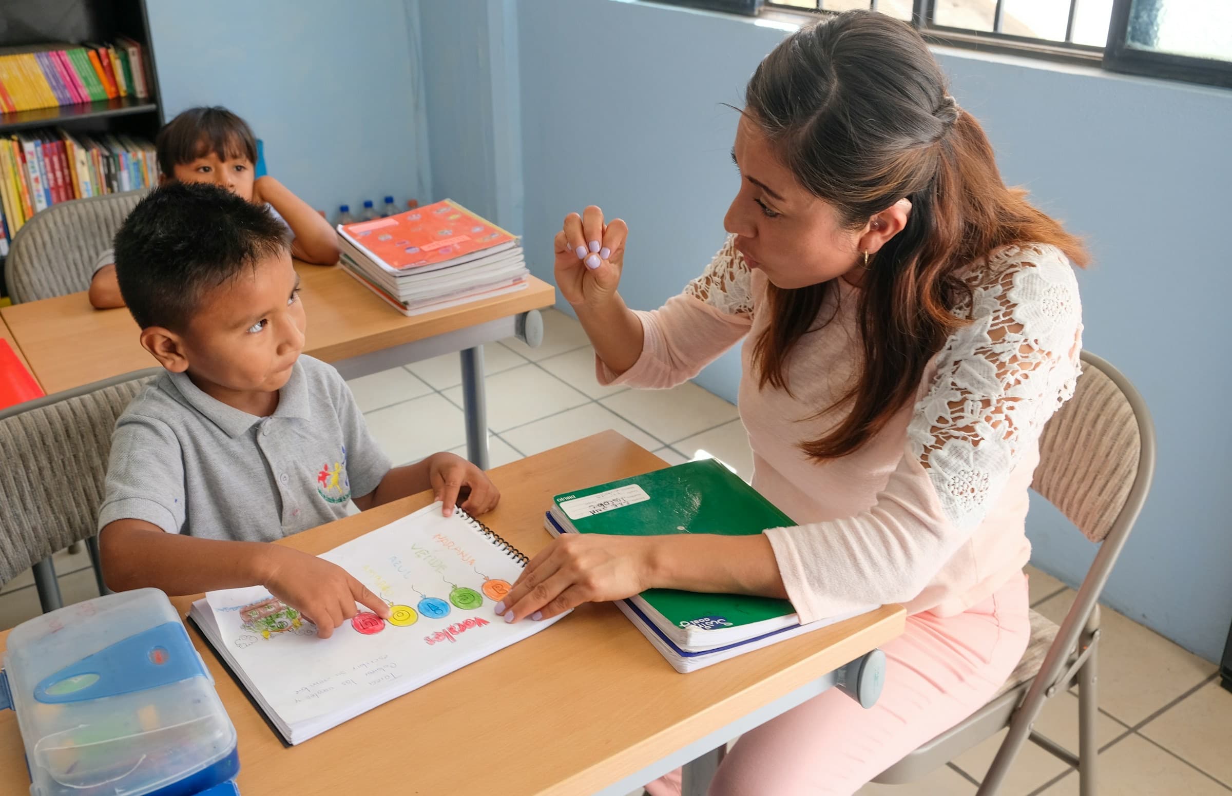 A tutor pointing to a workbook while a young student follows along
