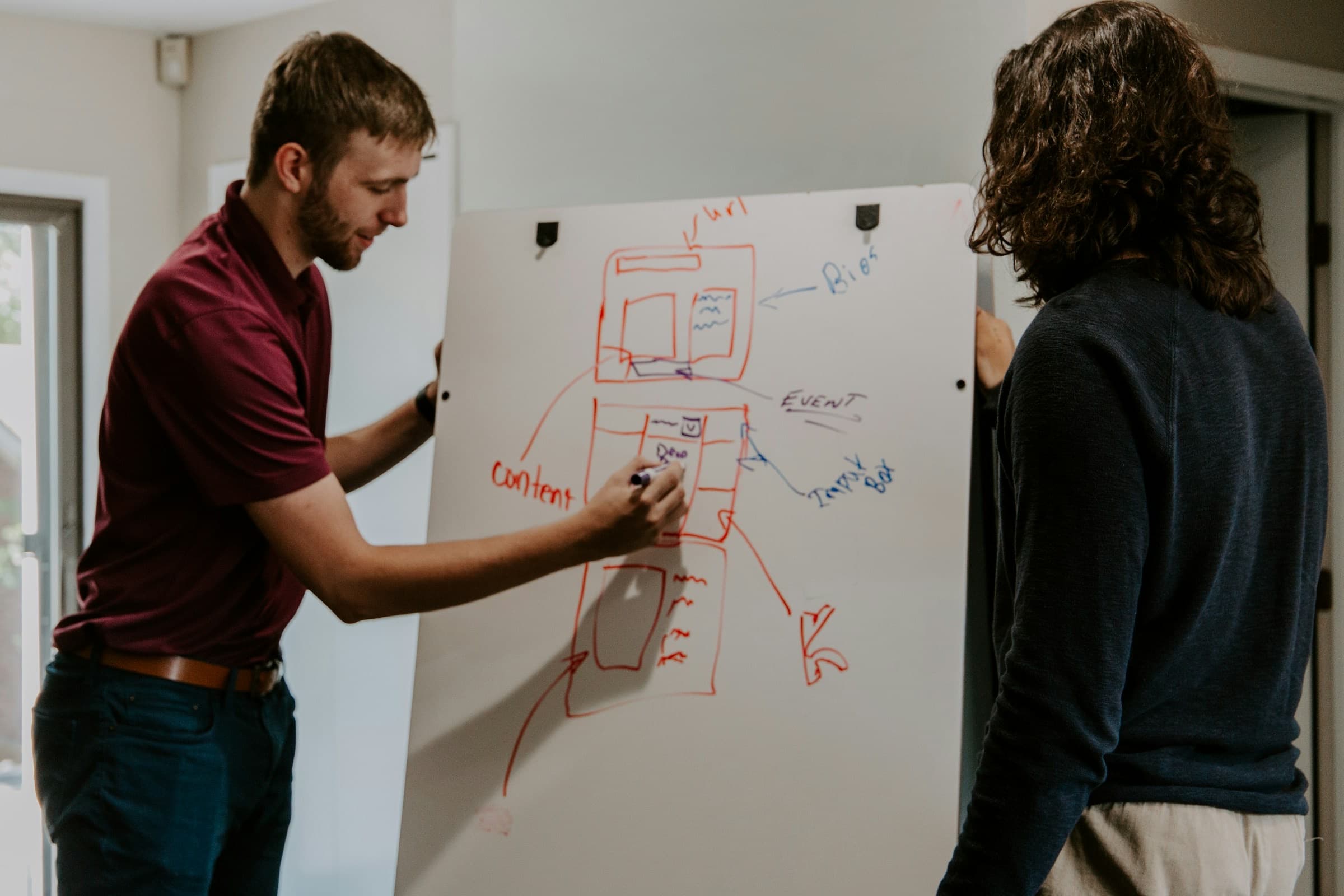 A tutor sketching an explanation on a whiteboard while a student watches